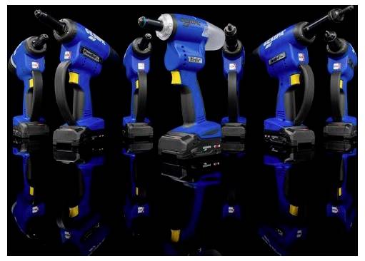 Four blue and black cordless power tools with batteries are reflected on a glossy black surface, suggesting professional use.