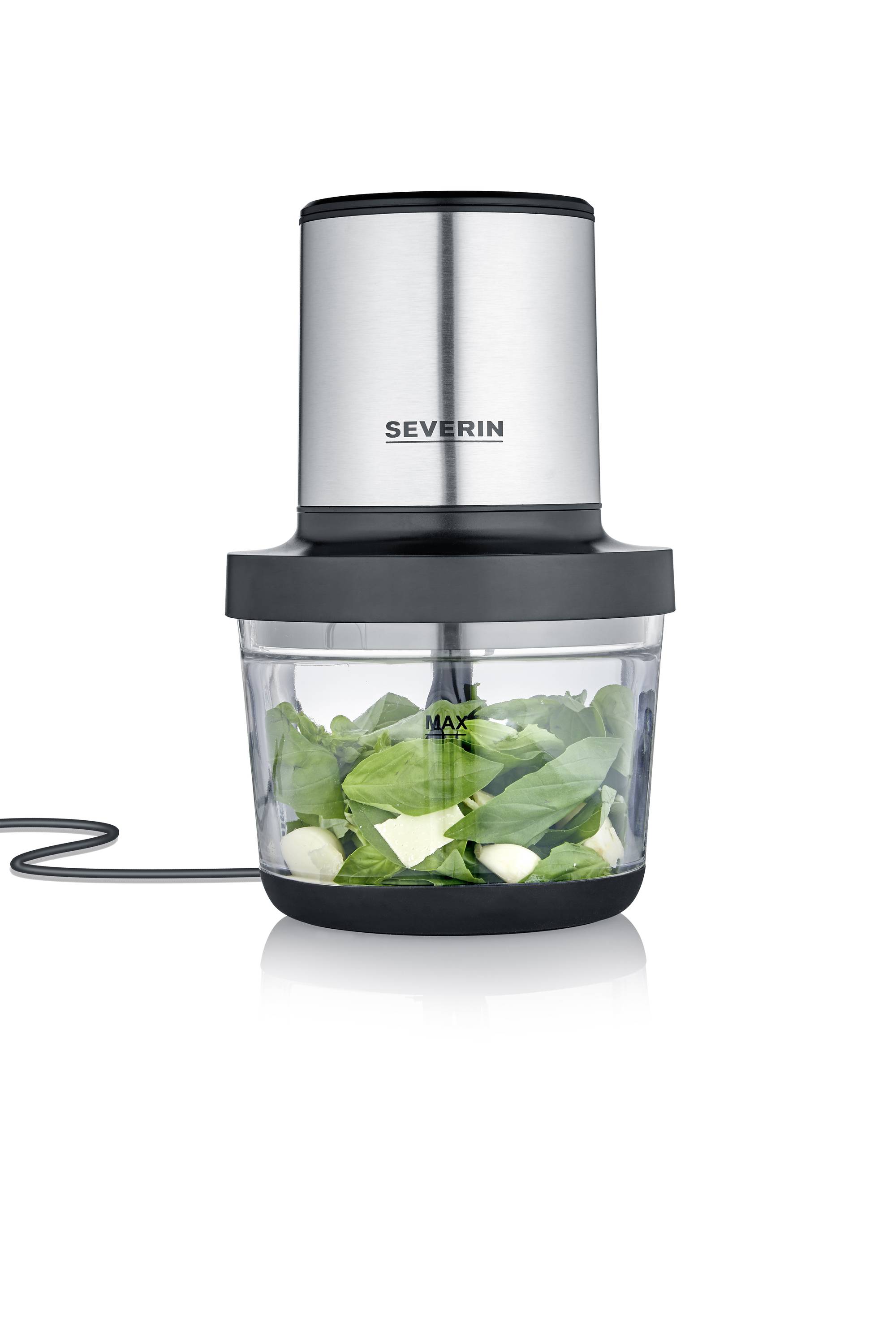 An electric blender with a stainless steel casing, filled with fresh green leaves and garlic cloves in a glass container.
