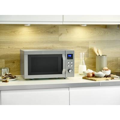 A silver microwave sits in a modern kitchen. To its right are a milk bottle, eggs, and a chopping board.