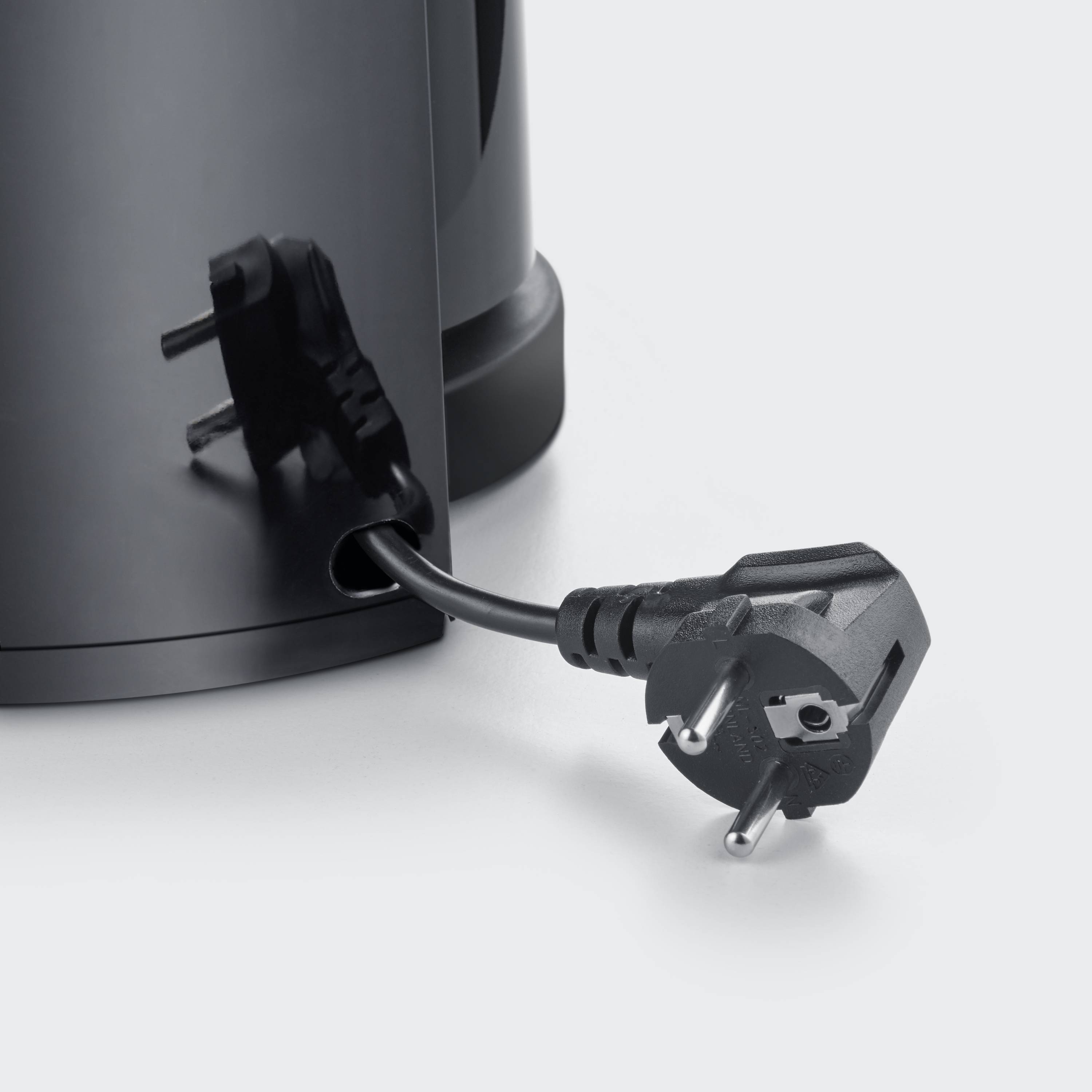 A black power cable is plugged into a cylindrical, black coffee machine that is sitting on a grey surface.