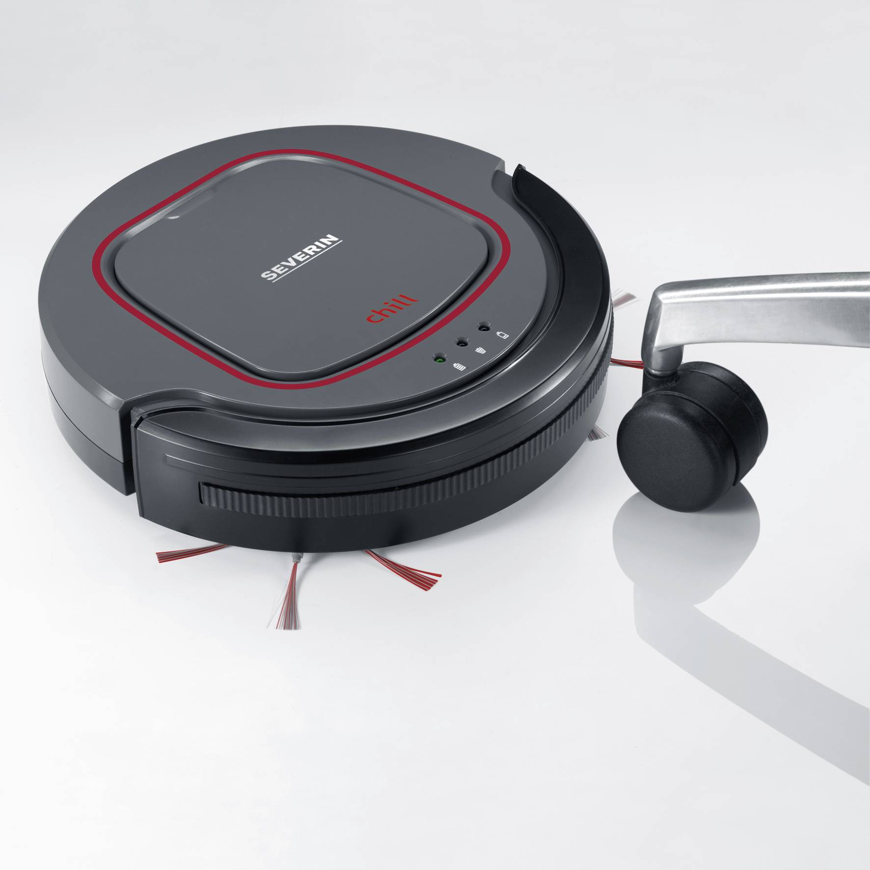 A black, round robot vacuum with red details, sitting on a floor next to a chair leg.