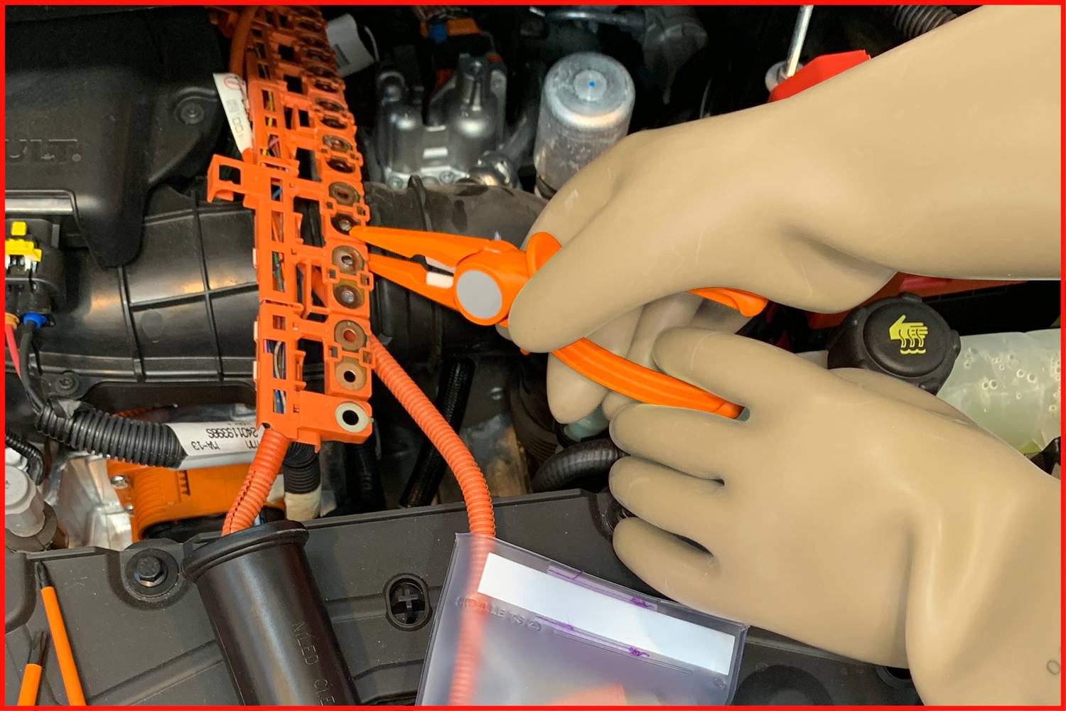 A person wearing gloves is working on electrical cables in a vehicle's engine compartment.