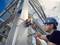 A worker is wearing a blue hard hat and securing a device to a steel structure outdoors using a tool.