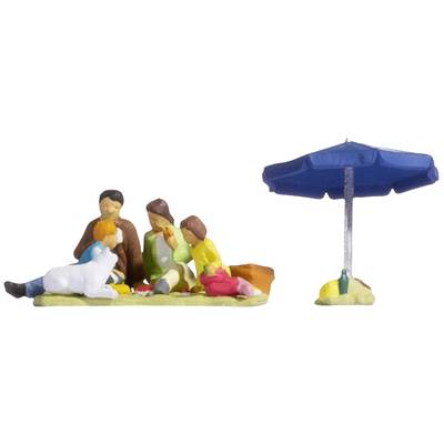 A family with a dog is sitting under a blue parasol on a blanket.