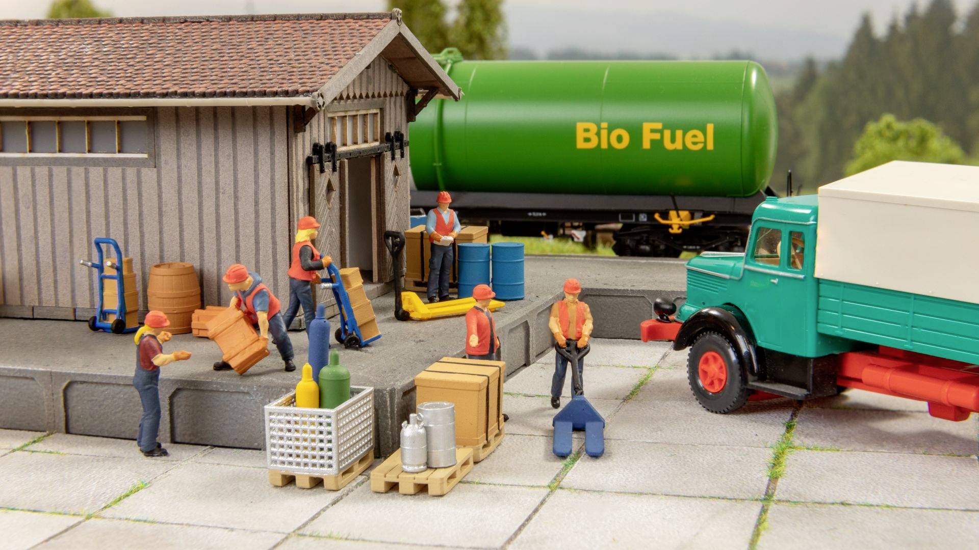 Figures loading and unloading cargo at a warehouse. A green tank with 'Bio Fuel' inscription stands in the background.