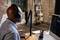 A person wearing headphones is speaking into a microphone in a studio. A computer screen displays audio software.