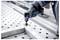 Gloved worker uses a Bosch cordless power tool to fasten a metal sheet on a perforated industrial worktable.