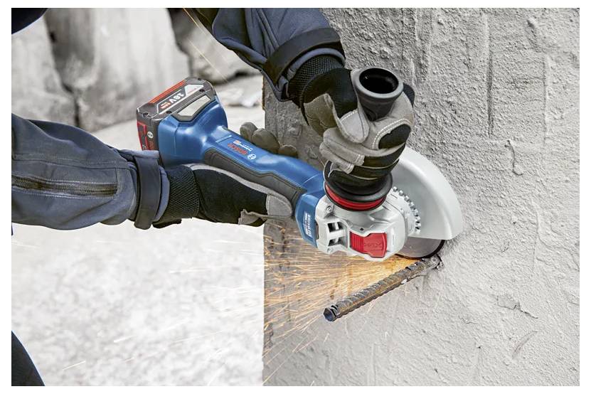 A person uses a blue handheld power grinder to cut through a metal rebar protruding from a concrete wall, with sparks flying.