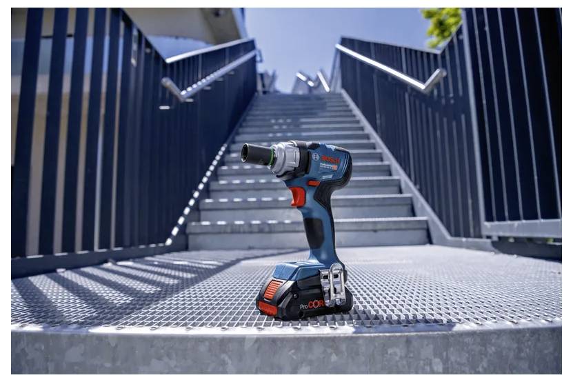A cordless power drill with a blue and black design resting on metal steps, with a modern building and blue sky in the background.