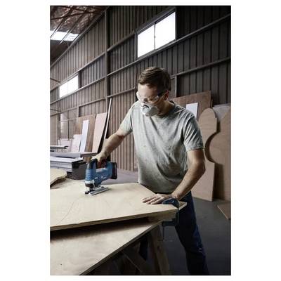 Person wearing safety gear uses a jigsaw on plywood in a woodworking shop.