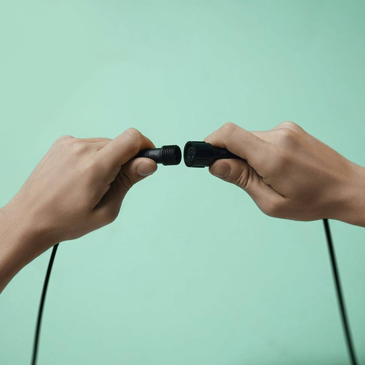 Two hands are connecting a black cable with a plug and a socket against a green background.