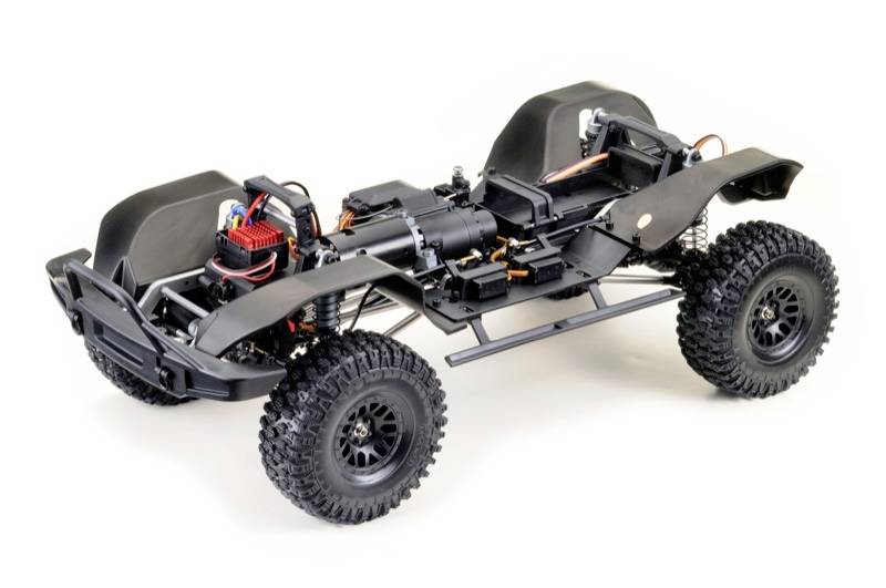 The image depicts a remote-controlled car chassis without bodywork, with visible electronics and chunky tyres.