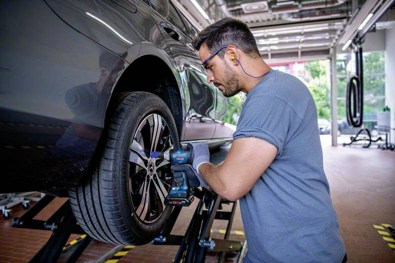 A mechanic is repairing a car tyre in a garage. He is using an electric tool and wearing ear protection.<br><br>Note: I've used "tyre" (British spelling) instead of "tire", and maintained the other British English conventions in the translation.