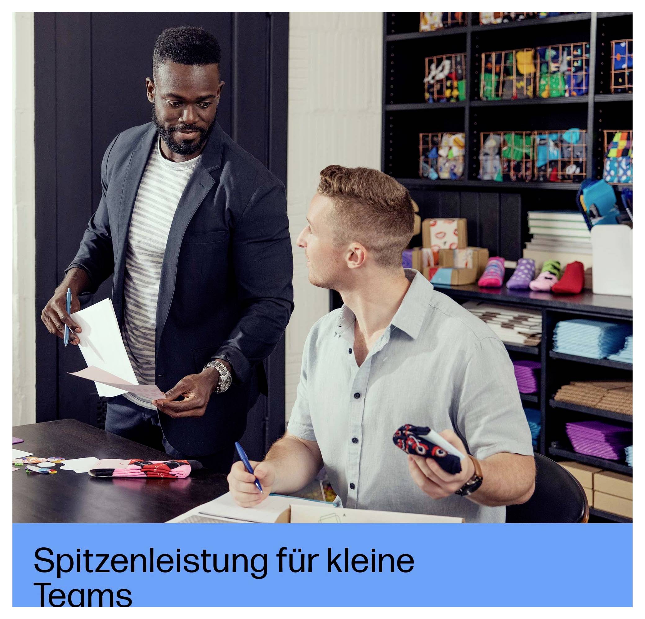 Two coworkers review papers and a phone in a fabric or print shop, with shelves of colorful materials behind them.