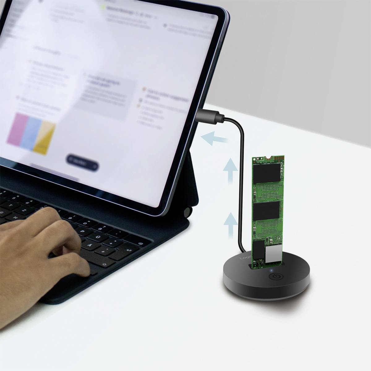 Tablet connected to external storage device. A hand typing on the tablet's keyboard. Connection cable from tablet to device.