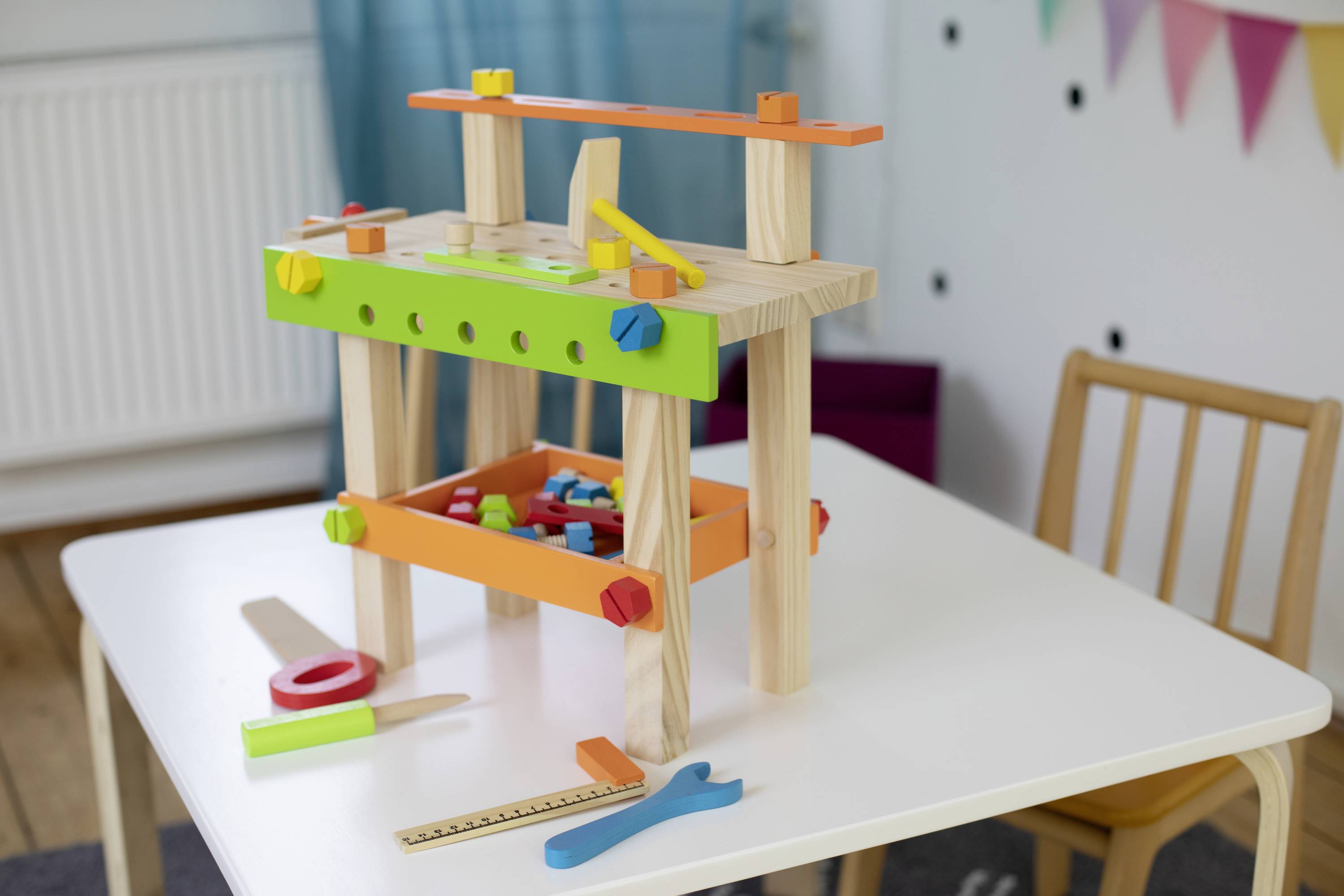 A colourful wooden toolbox on a table. Contains screws, nuts and tools in bright colours for children.