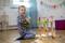 A smiling child sits on the floor playing with a colourful wooden workbench. Colourful bunting hangs on the wall in the background.