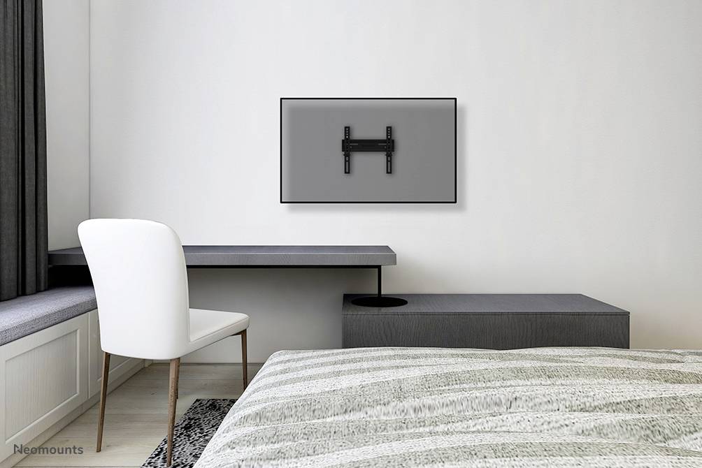 An empty television mount on a grey wall above a minimalist desk in a modern bedroom.