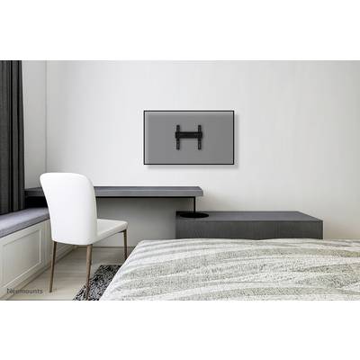 An empty television mount on a grey wall above a minimalist desk in a modern bedroom.