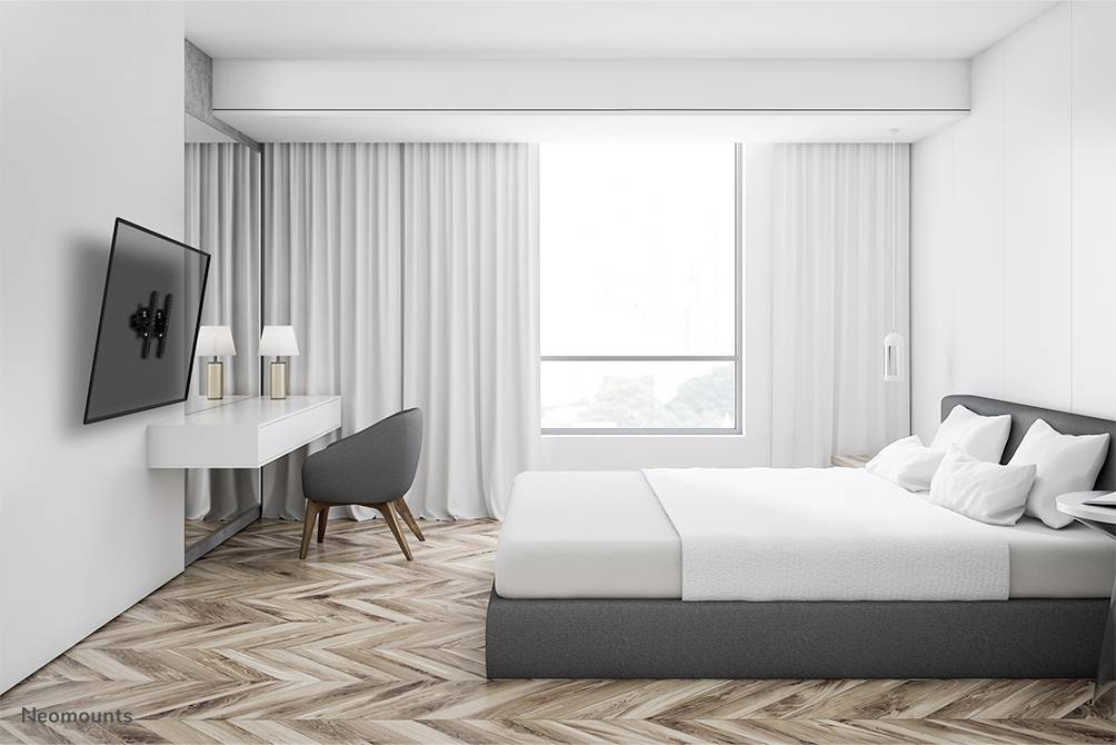 A modern bedroom with a large bed, a desk and a chair. A large window provides daylight, with curtains beside it.