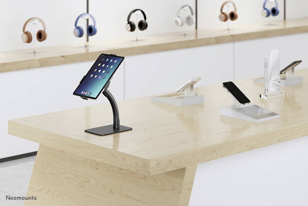 A sales area with multiple tablets and headphones displayed on a wooden table. One tablet is highlighted on a stand.