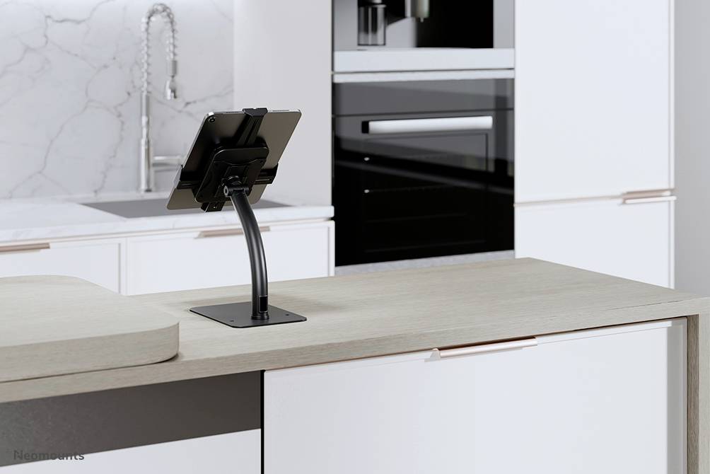 A tablet stands on a holder on a modern kitchen island with white and black design, with a sink visible in the background.