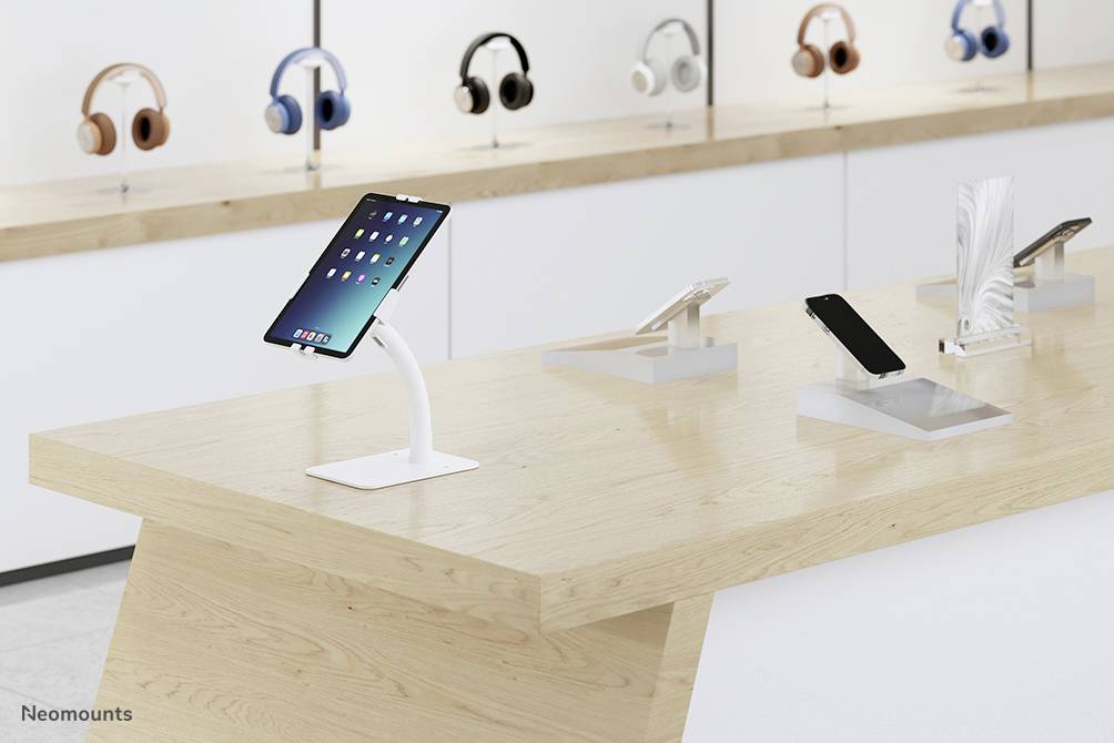 A modern electronics shop with tablets and smartphones displayed on a wooden display table, with headphones on shelves in the background.