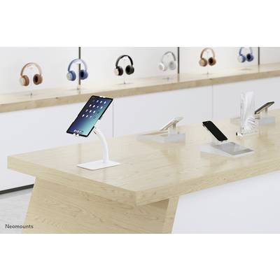 A modern electronics shop with tablets and smartphones displayed on a wooden display table, with headphones on shelves in the background.
