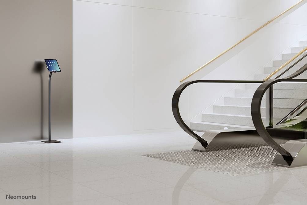 A digital information kiosk with a tablet stands next to a modern staircase in a bright, minimalist space.
