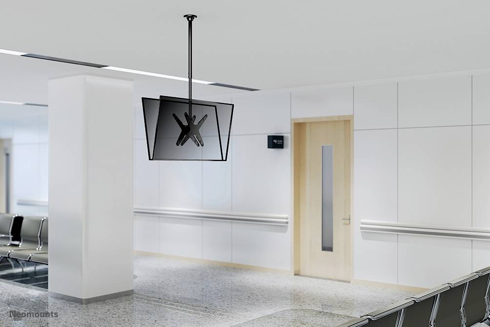 An empty waiting area with white walls and modern chairs. A flat-screen monitor hangs from the ceiling. Doors and signs are visible.