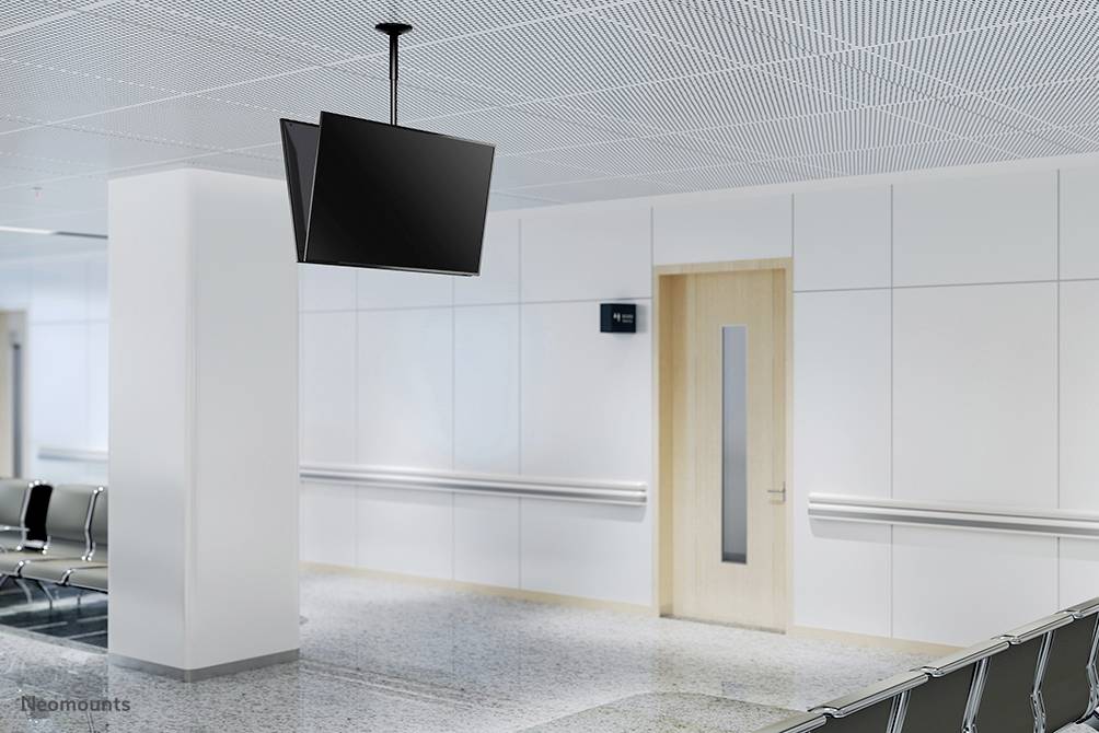 Empty waiting room with white walls, linoleum floor, black chairs along the wall and a flat-screen display on the ceiling.