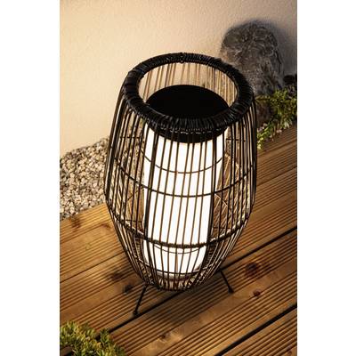 A stylish lamp on a wooden floor outdoors, surrounded by gravel and plants, glows softly in the darkness.