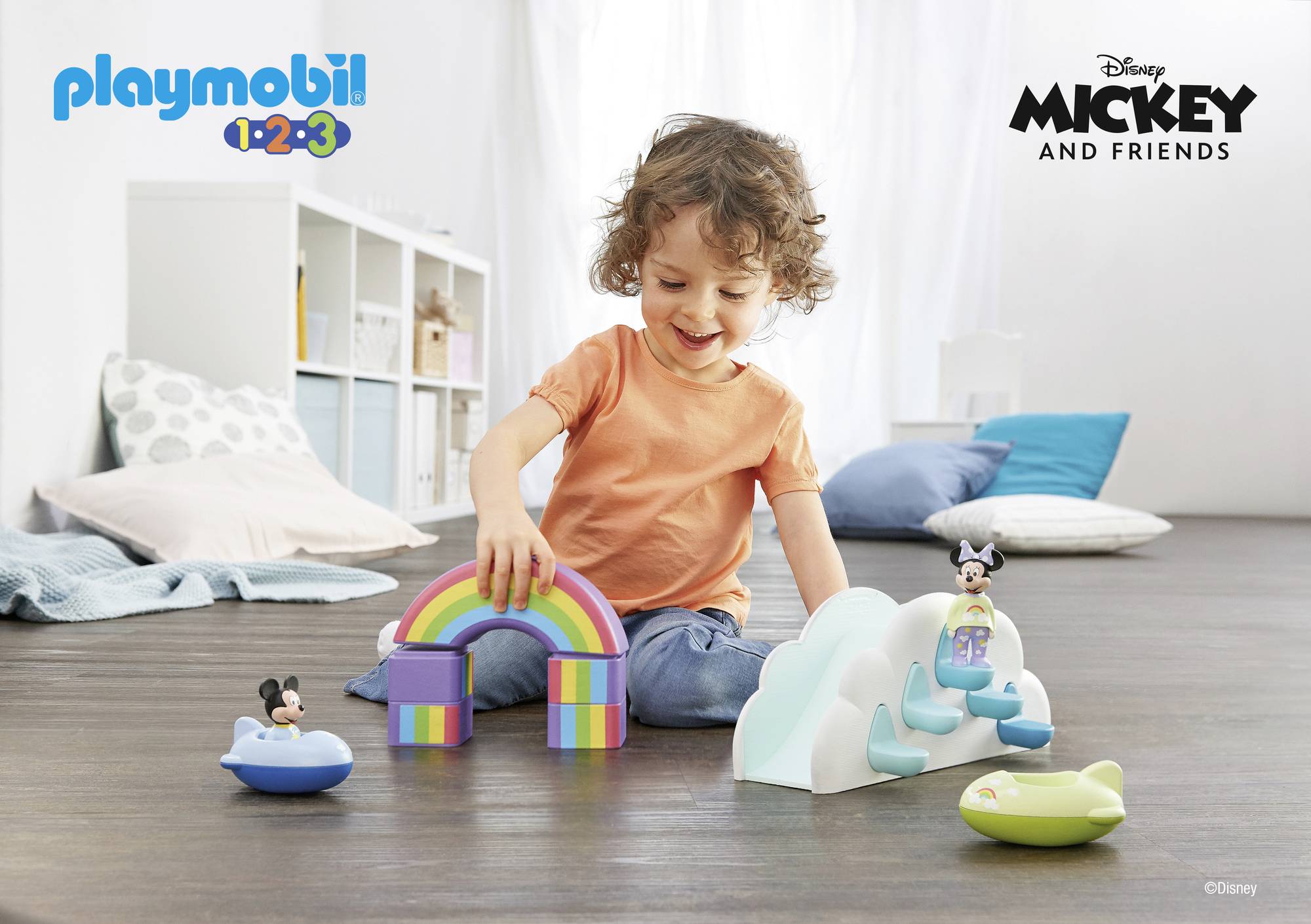 A child is happily playing with Playmobil toys, including rainbow blocks and Mickey and Minnie Mouse figures on a cloud slide.