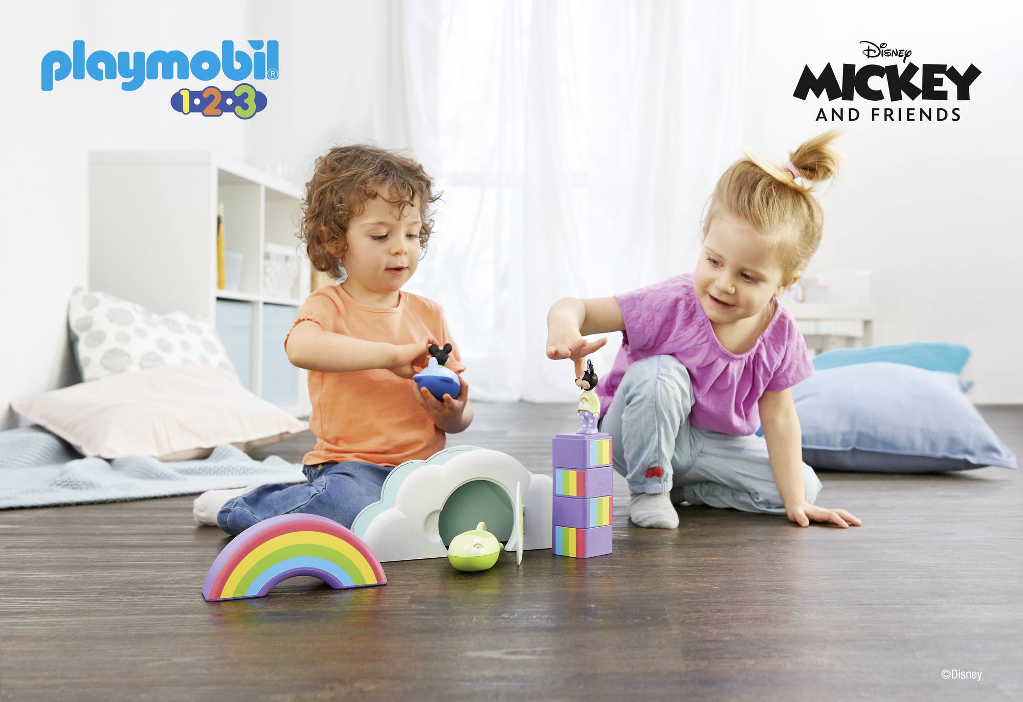 Two children are playing with colourful toys on a wooden floor. On the left is a boy wearing orange, on the right a girl in purple. At the top are the logos for 'Playmobil 1.2.3' and 'Disney Mickey and Friends'.