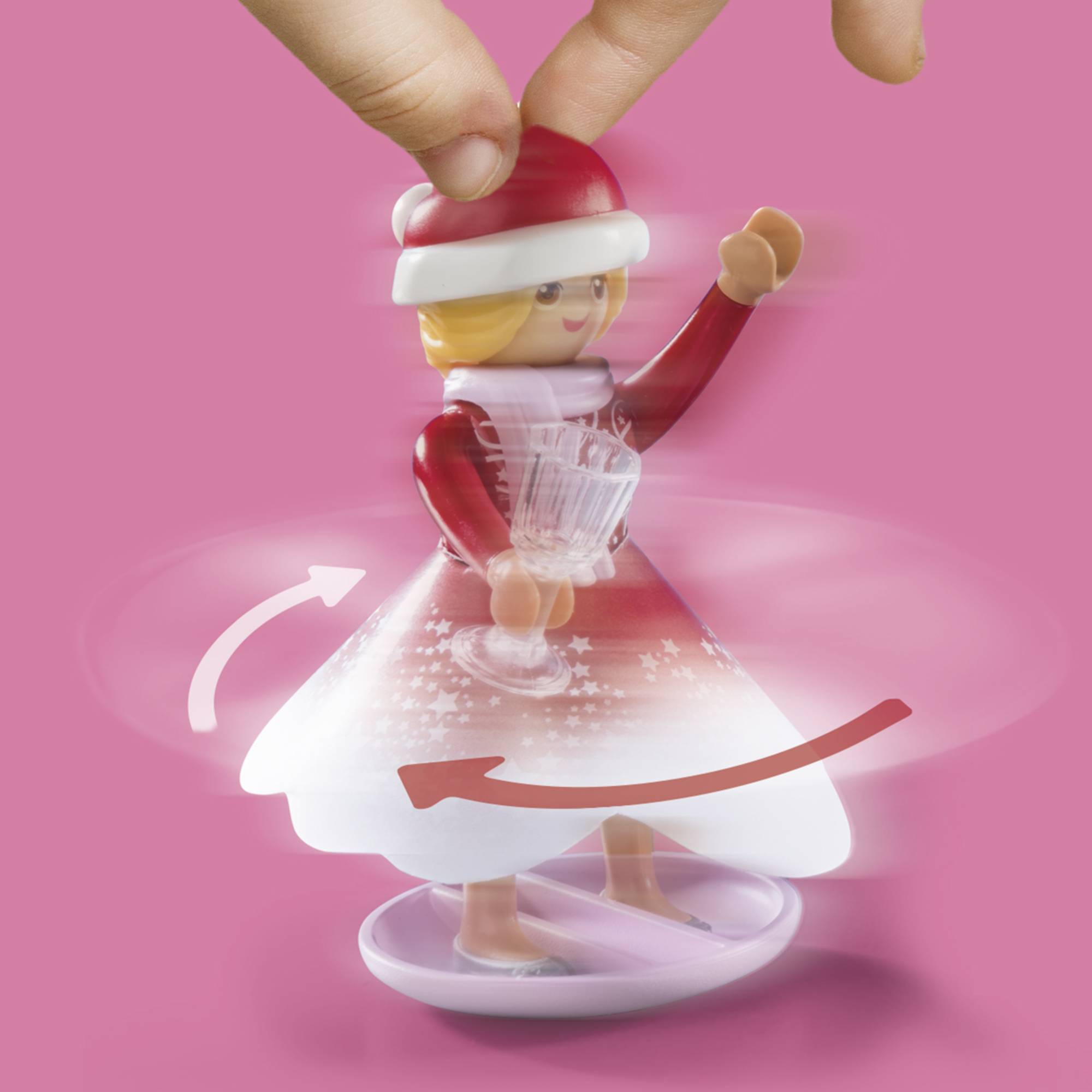 A red and white figurine in a rotating skirt, showing a snowflake and being turned by two fingers. Pink background.