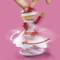 A red and white figurine in a rotating skirt, showing a snowflake and being turned by two fingers. Pink background.