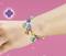 A hand is wearing a colourful bracelet with various charms on a pink background.
