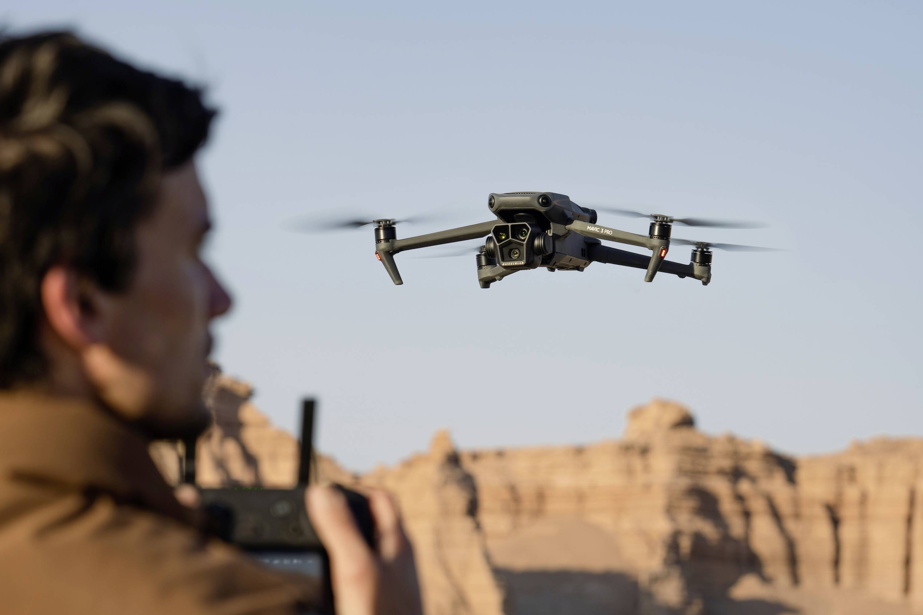 A person is controlling a drone with a remote control in a rocky desert landscape.