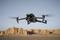 A drone flies in the desert, with rock formations visible against a clear sky in the background.