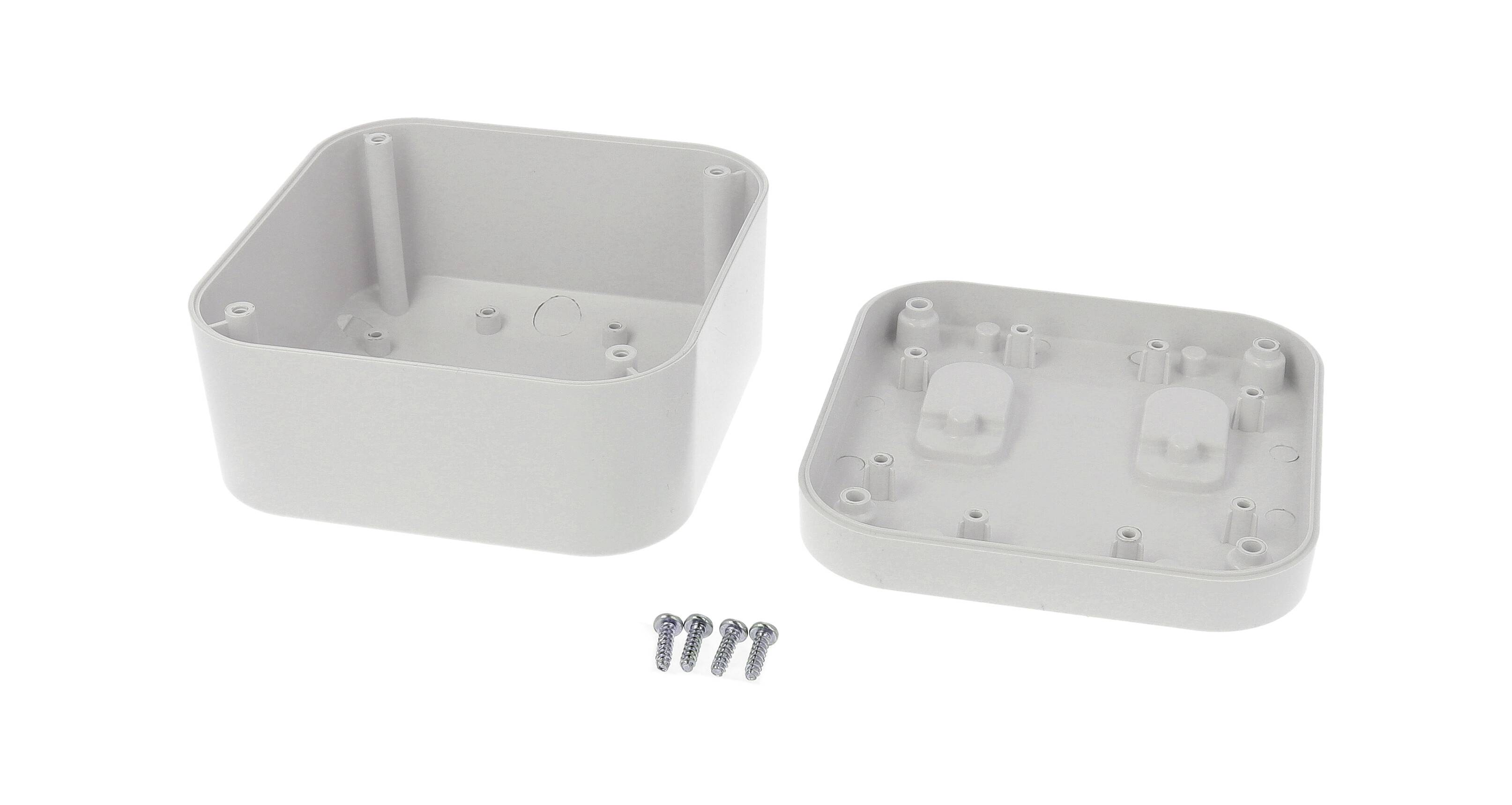 A rectangular, grey plastic enclosure, opened. Contains four screws lying beside the housing.