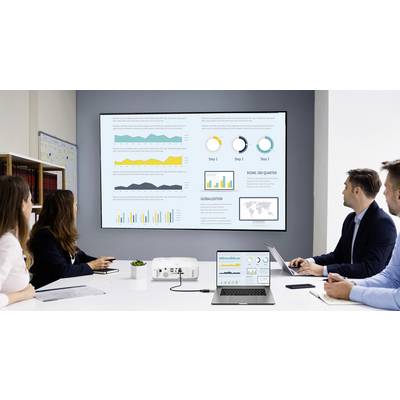 A team of four people is sitting in a conference room, examining a wall presentation with graphs and diagrams.