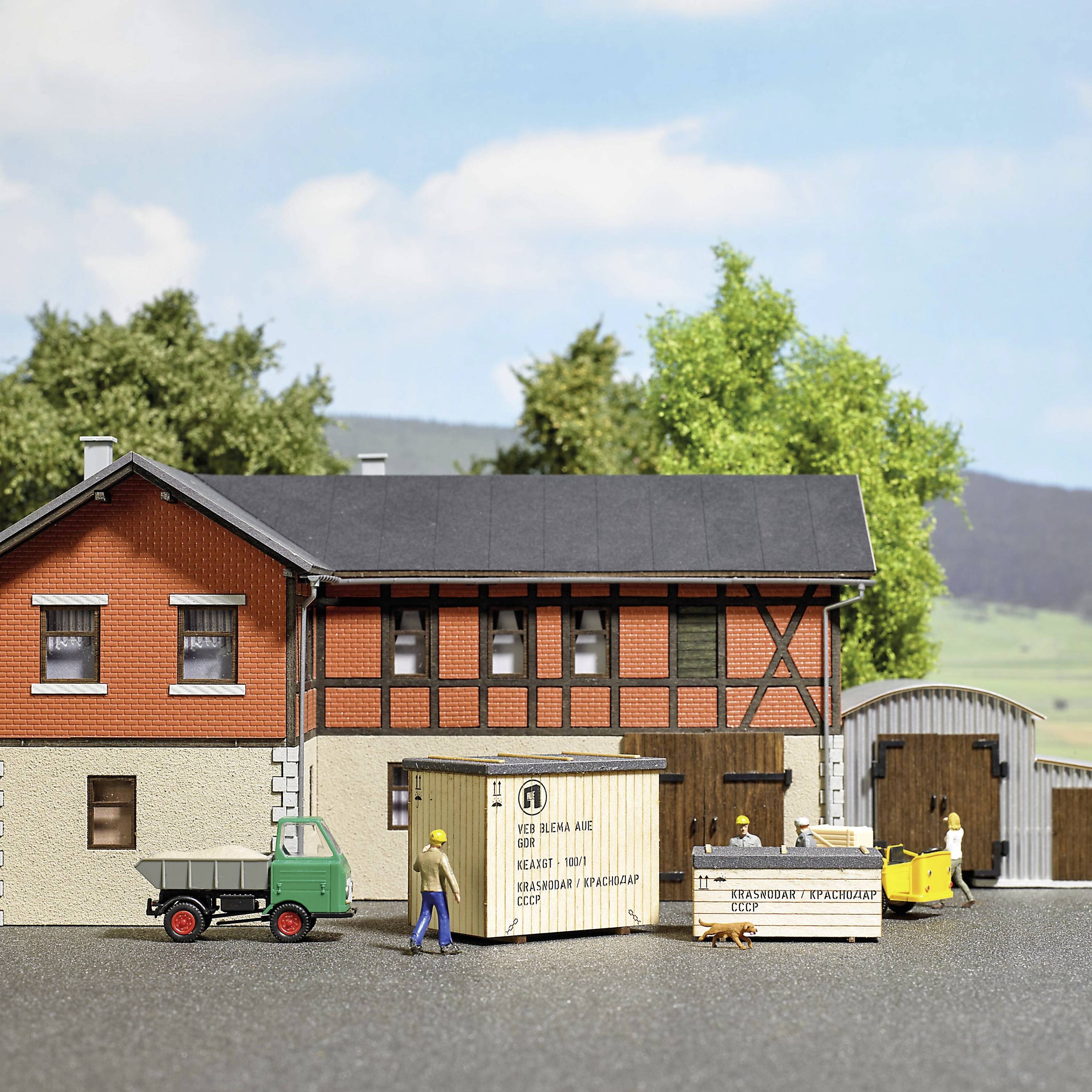 A miniature landscape depicts a two-storey half-timbered building with a red façade. A mini lorry and figures stand in front of it.