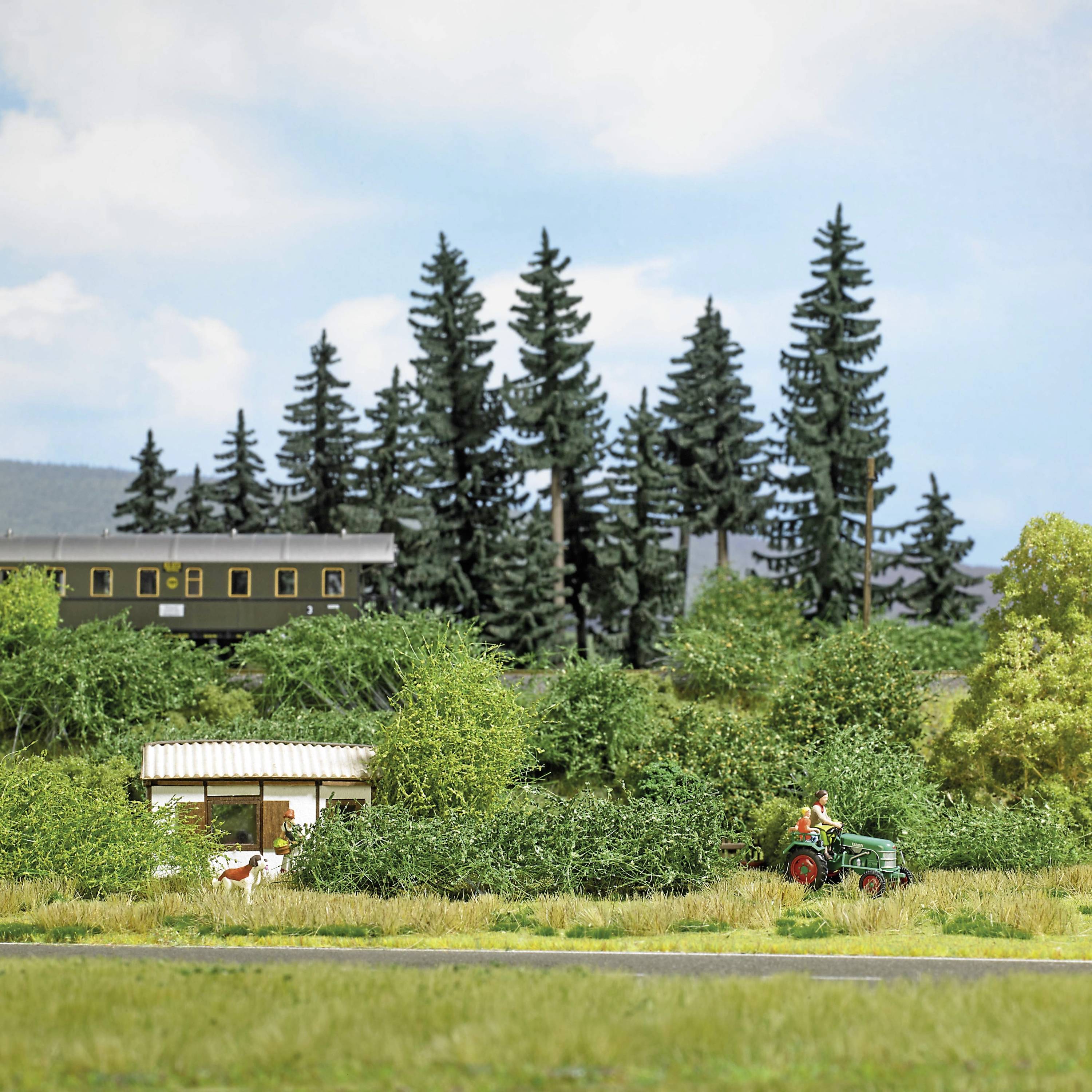 Model landscape with trees, a barn and a tractor with a farmer in a field. Behind it, a building, sky with clouds.