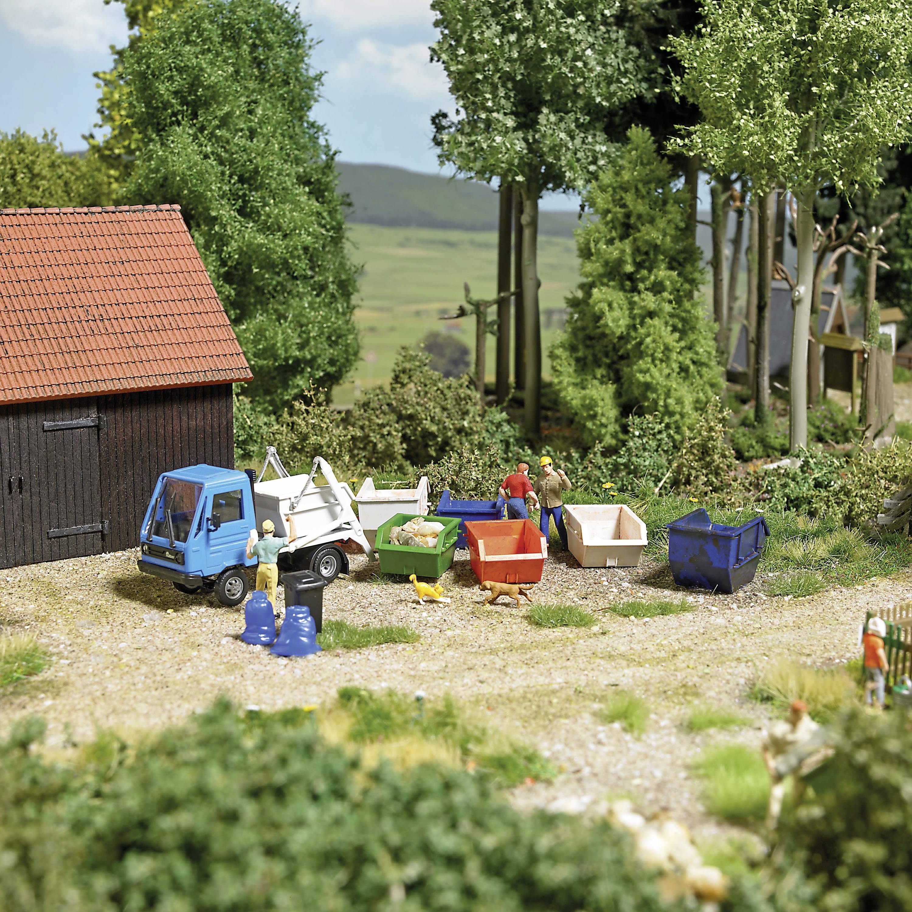 A miniature scene of a recycling centre in the countryside with small figures sorting waste into differently coloured containers.