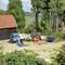 Several miniature people surrounded by trees, working in a yard with various colourful containers.