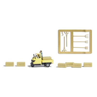 A miniature figure is driving a yellow three-wheeled vehicle and transporting hay bales. To the right, a cast frame with tools.