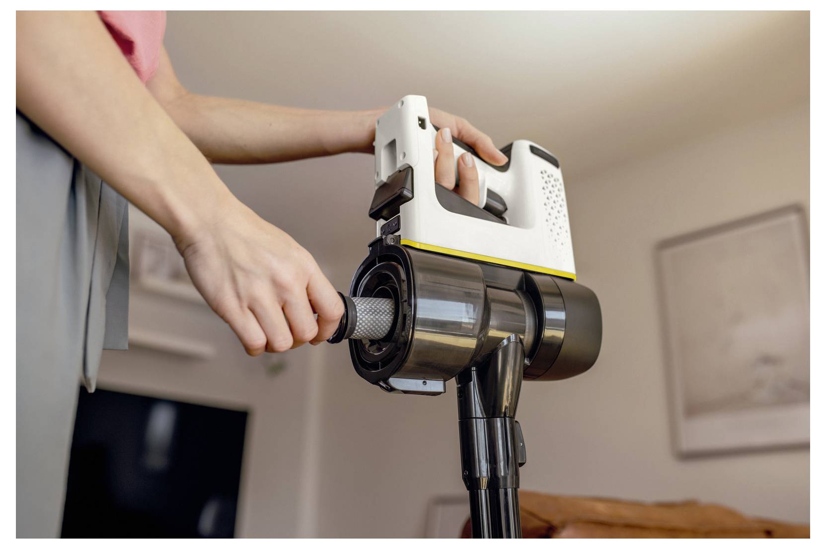 A person inserts a filter into a handheld vacuum cleaner, demonstrating a maintenance step in a home setting with soft-focus background.
