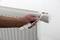 A hand is holding a radiator thermostat with an adjustment tool being fitted to a radiator.