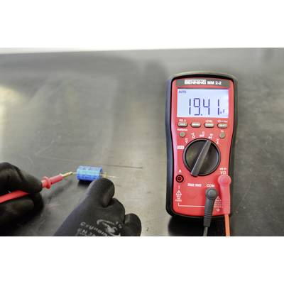 A red multimeter displays '19.41' on a digital display. A hand holds a testing probe connected to a blue electronic component.