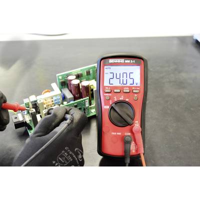 A person is measuring the voltage of a circuit board with a digital multimetre, which displays 24.05 V.